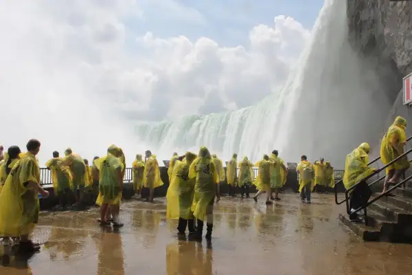 Tłum turystów w żółtych płaszczach przeciwdeszczowych podziwia potęgę wodospadu Niagara. Ciekawe informacje o tym miejscu czekają na odkrycie.