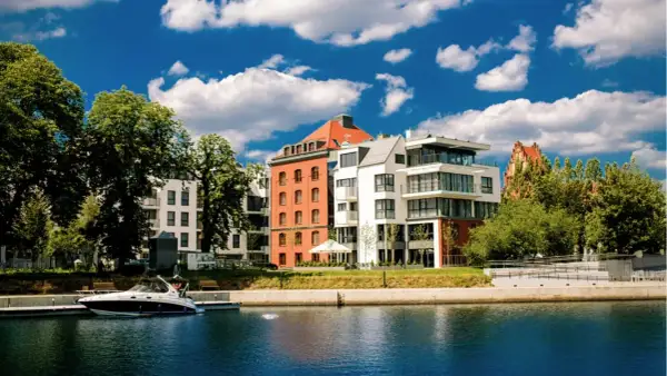 Nowoczesne budynki nad wodą, przypominające hotel Almond, z łodzią przy nabrzeżu i błękitnym niebem.