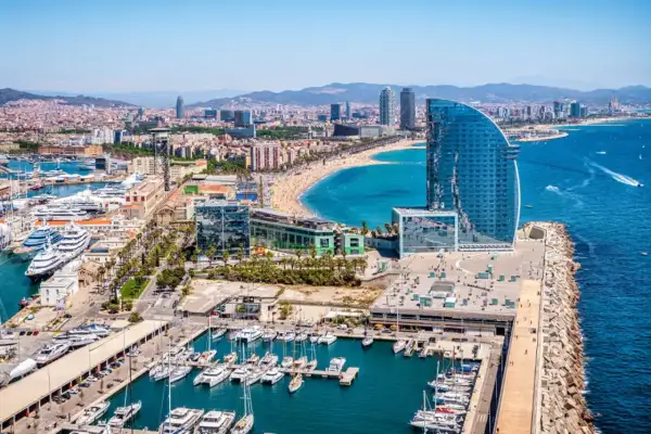 Widok na Barcelonę i jej piękne morze, z luksusowymi jachtami w porcie i nowoczesnym hotelem w kształcie żagla.