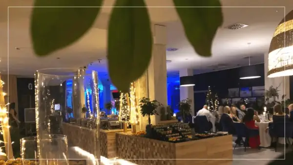 Elegancki sylwester w hotelu. Goście siedzą przy stołach, w tle bufet z przekąskami i świąteczne dekoracje.