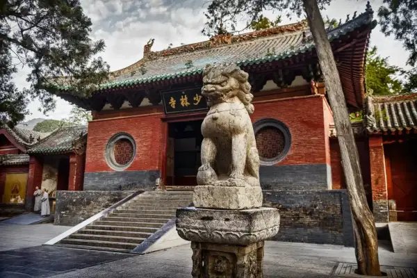 Kamienny lew strzeże wejścia do klasztoru Shaolin. Dwie postacie w szatach mnichów zbliżają się do schodów.