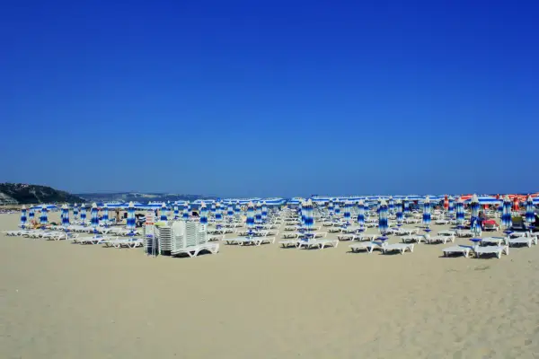 Plaża w Albena Bułgaria, rzędy leżaków i parasoli w niebiesko-białe pasy pod błękitnym niebem.