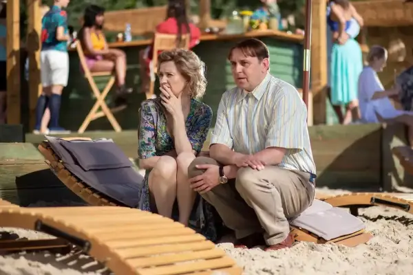 Para zmartwiona siedzi na plaży, jakby czekała na przyjazd teściów w hotelu z teściowie 2.